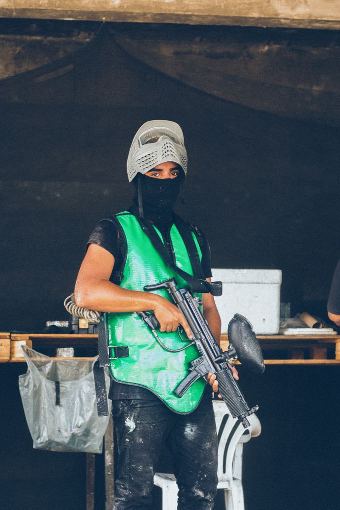 A paintball player wearing a green vest and helmet, holding a paintball marker indoors.