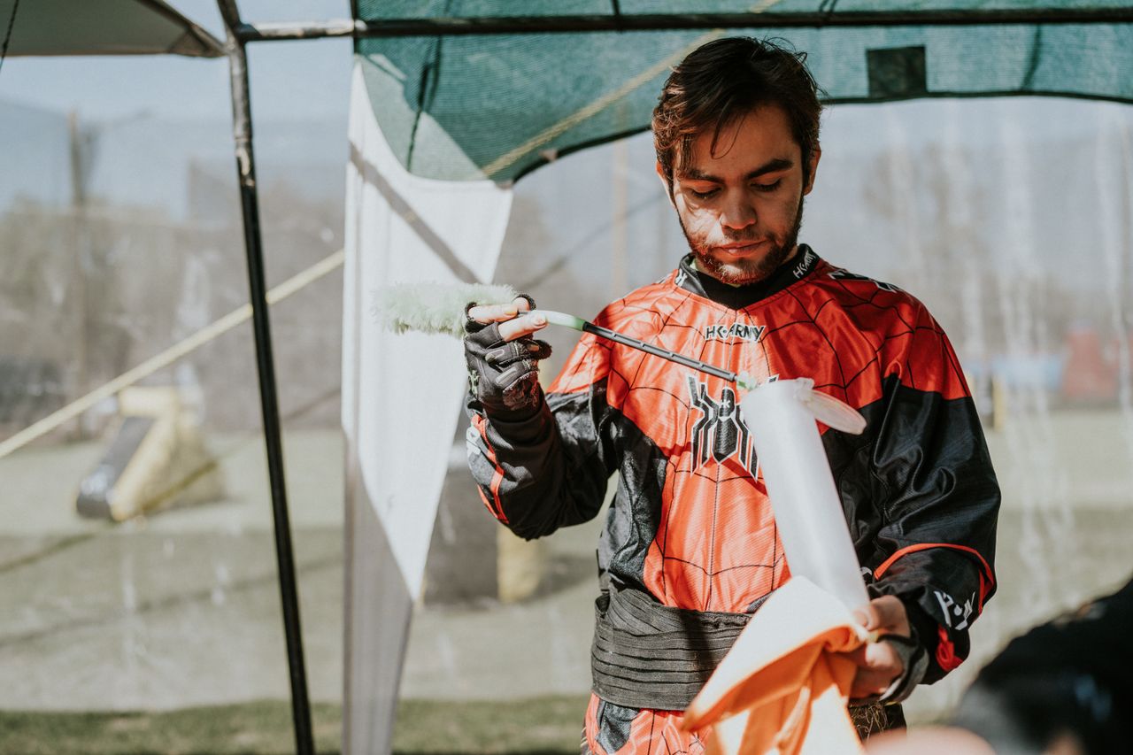 A man in sportswear cleans his paintball gun outside on a sunny day, preparing for action.