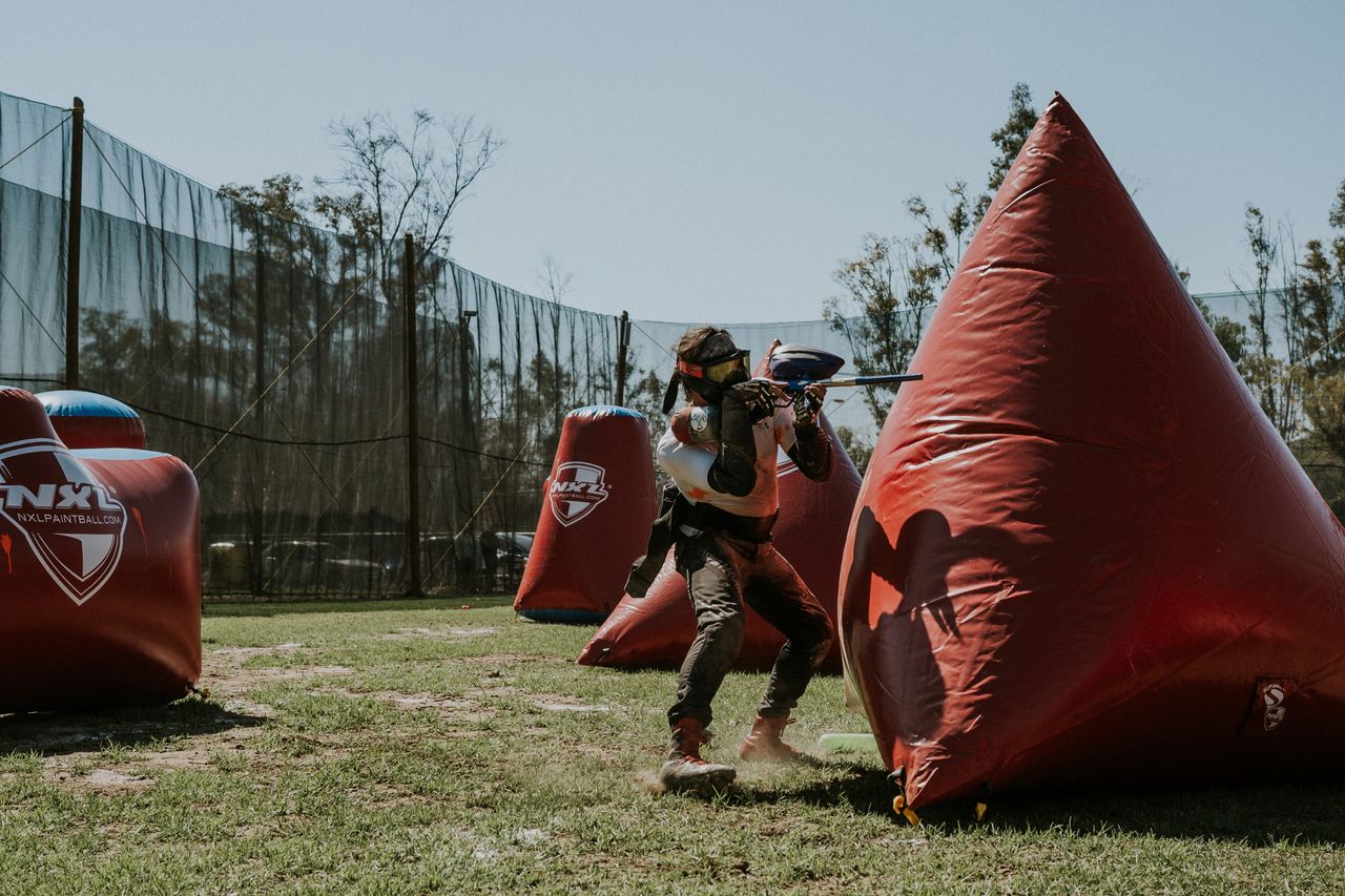 A person actively playing paintball outdoors, aiming behind inflatable covers.