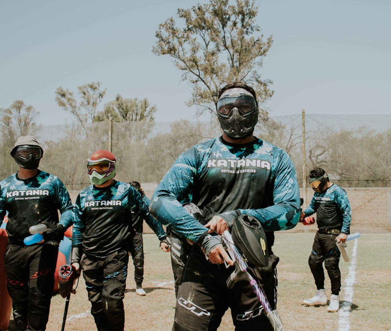 Group of men playing paintball outdoors, wearing protective masks and gear.