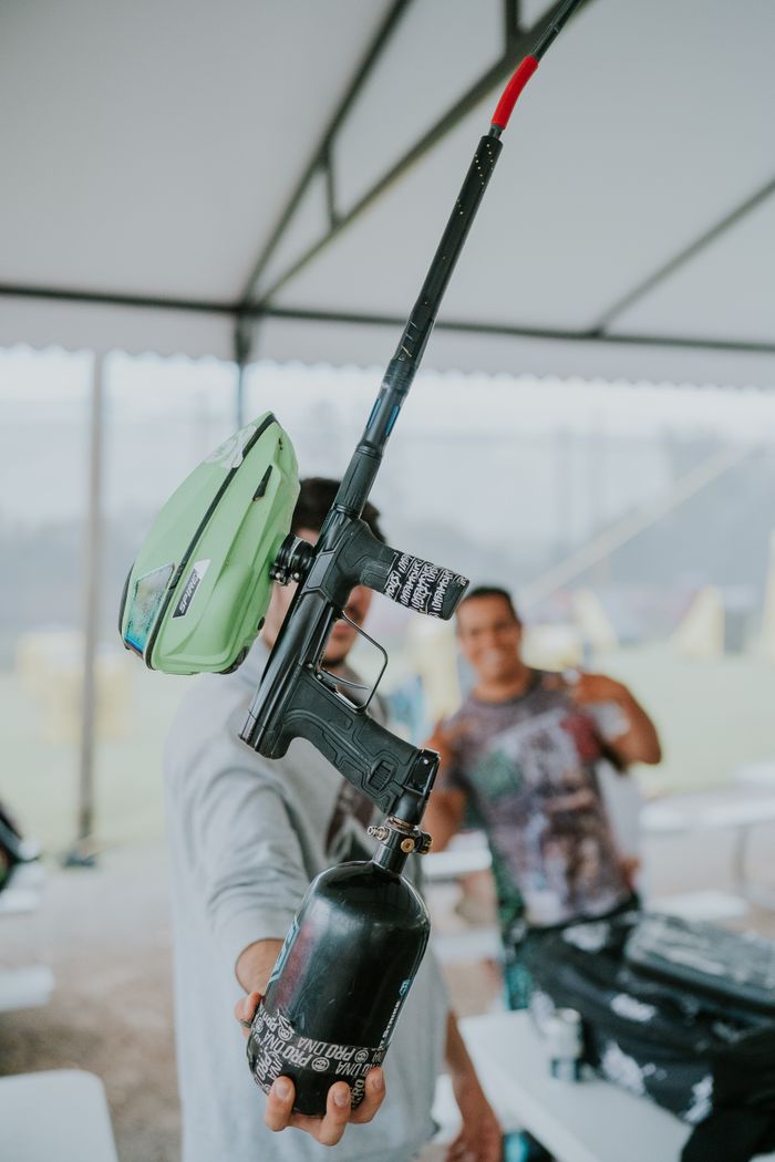 Person holding a paintball gun indoors, with a focus on equipment and blurred background.